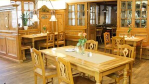 Comedor tradicional con mobiliario de madera, que incluye una mesa grande y sillas, y una zona de cocina con armarios de madera y una ventana.