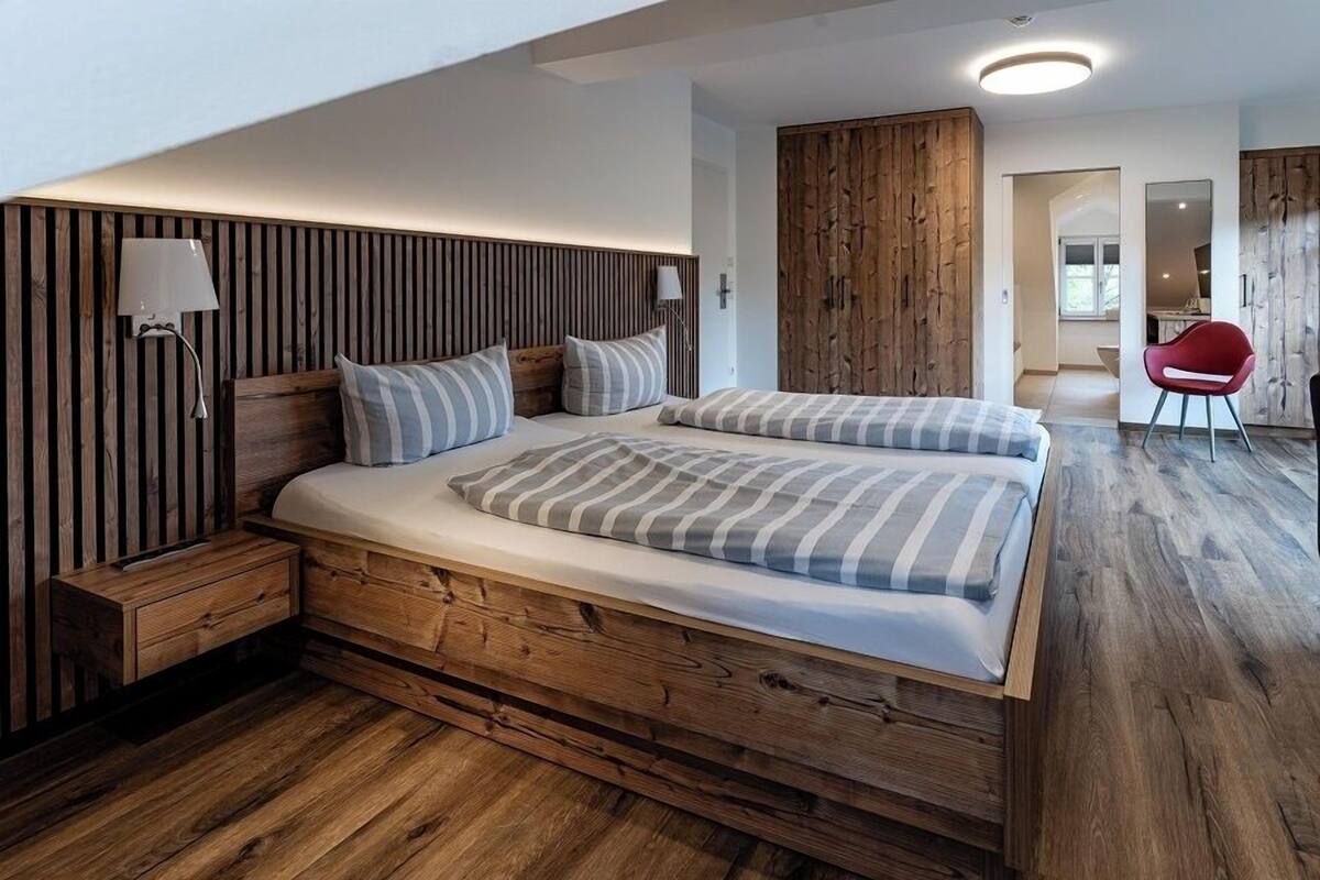 Une chambre moderne avec une tête de lit en bois, un grand lit avec une literie à rayures, une table de chevet et une chaise rouge dans un coin.