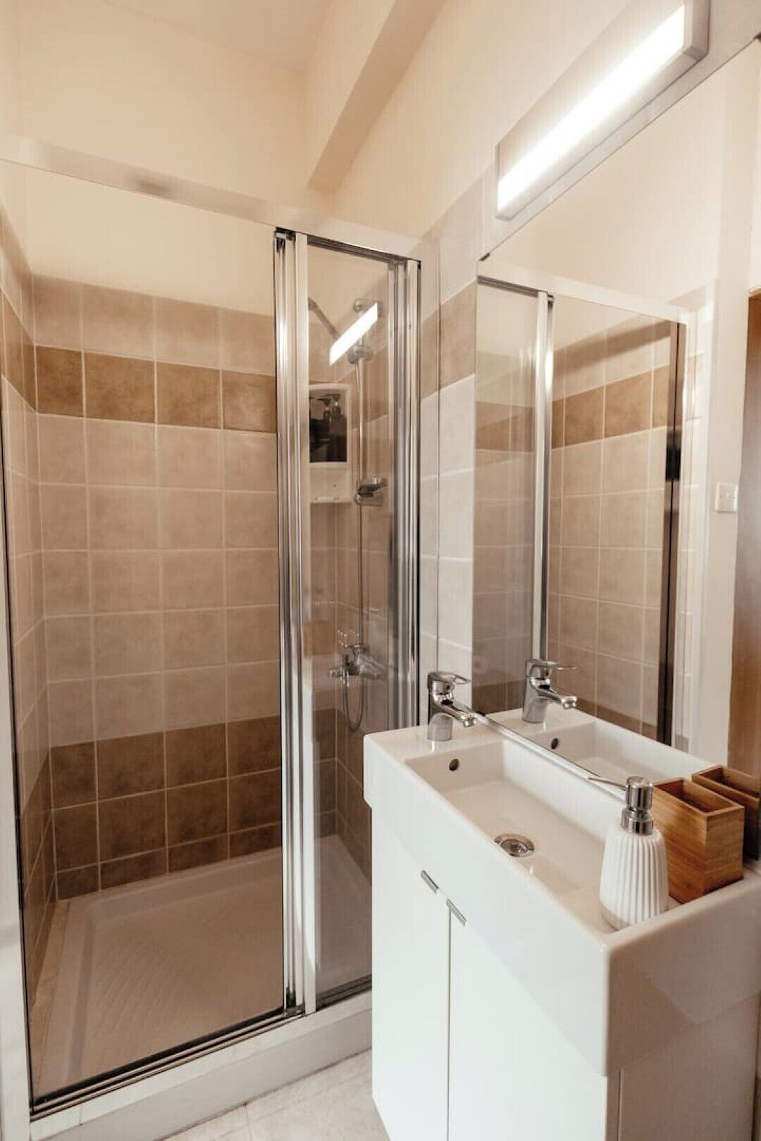 Un baño moderno con ducha envuelta en vidrio, tocador blanco y un espejo grande.