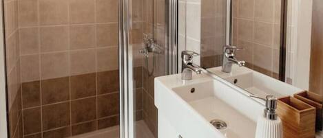 Un baño moderno con ducha envuelta en vidrio, tocador blanco y un espejo grande.