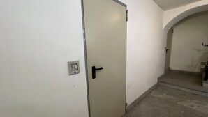 Un pasillo con una puerta cerrada, un interruptor de luz y una escalera que lleva a otra habitación.