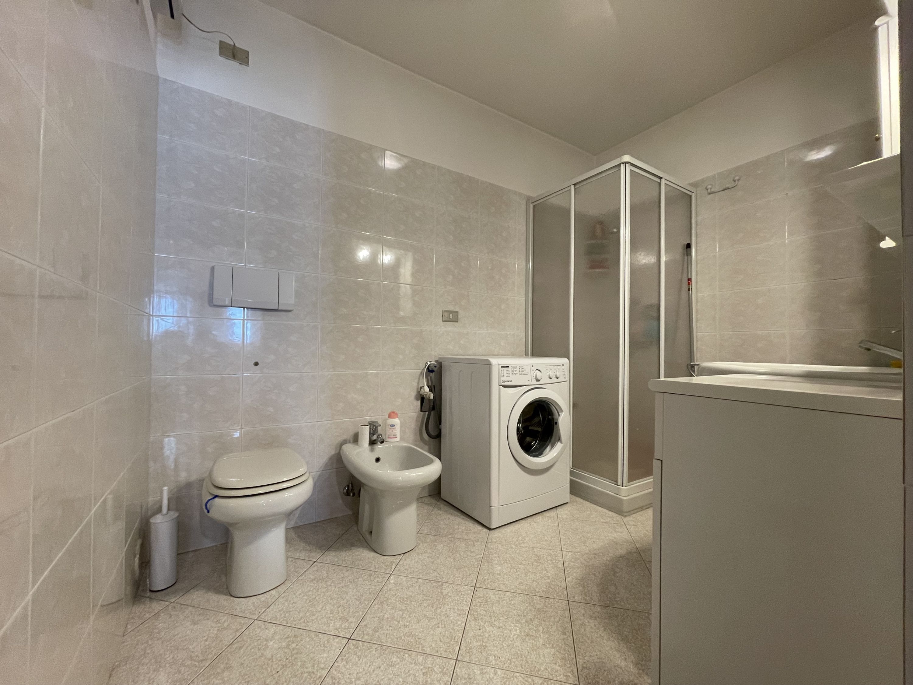 Ein modernes Badezimmer mit Toilette, Bidet, Waschmaschine und einer Duschkabine.