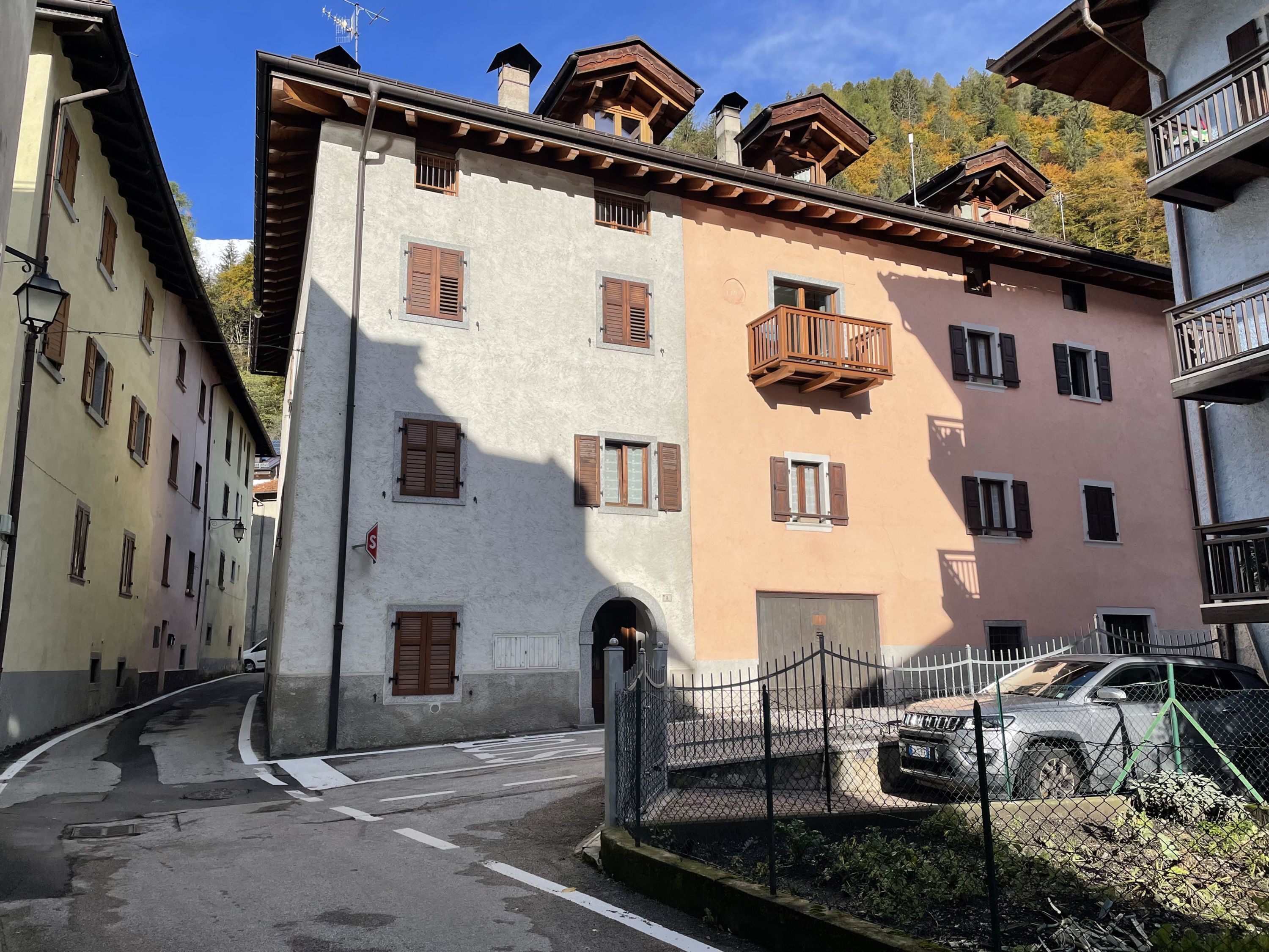 A multi-story building with a mix of balconies and windows, a gated entrance, and a parked car.