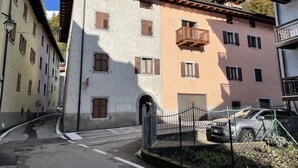 Un edificio de varios pisos con una mezcla de balcones y ventanas, una entrada con portón y un coche estacionado.