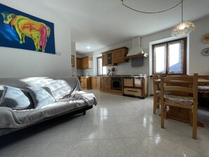 A modern living room with a sofa, a dining table with chairs, and a kitchen area with wooden cabinets and a stove.