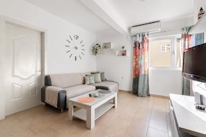 A modern living room with a sofa, coffee table, TV, and a wall clock.