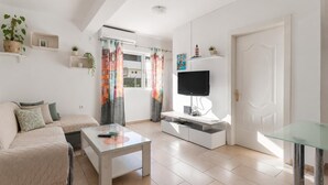 Ein modernes Wohnzimmer mit einer Couch, einem Glastisch, einem Fernseher auf einem weißen Schrank und einer Tür mit dekorativer Verkleidung.