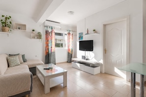 Ein modernes Wohnzimmer mit einer Couch, einem Glastisch, einem Fernseher auf einem weißen Schrank und einer Tür mit dekorativer Verkleidung.