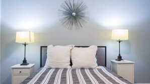 Un dormitorio con una cama, dos mesitas de noche y una lámpara fijada en la pared.