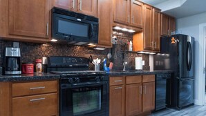Una cocina con armarios de madera, estufa negra, microondas y refrigerador.