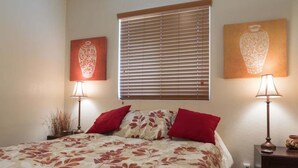 A bedroom with a bed, two bedside lamps, a window with blinds, and two wall-mounted paintings. - North Phoenix Condo – Sunset Views + Community Heated Pool (Phoenix)