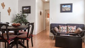 A living room with a dark-colored sofa, a coffee table, and a dining area with a round table and chairs. - North Phoenix Condo – Sunset Views + Community Heated Pool (Phoenix)