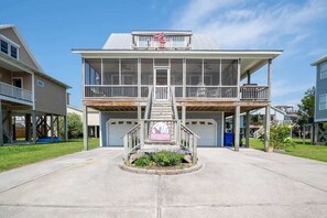 A two-story house with a covered front porch, a garage, and a small garden area in front. - Ruffians Roost (Carolina Beach)
