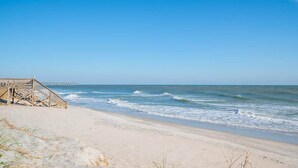 A beach with a wooden boardwalk leading to a pier. - Ruffians Roost (Carolina Beach)