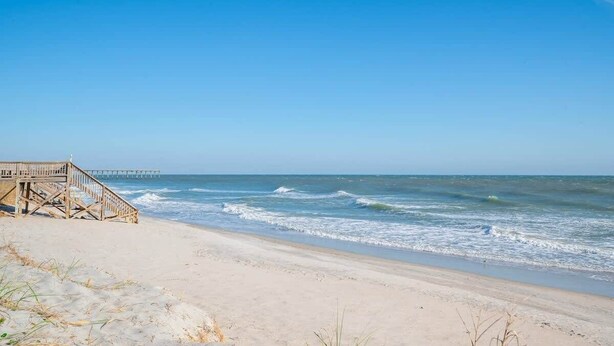 Een strand met een houten vlinderpad dat naar een steiger leidt.