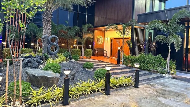 A modern building with a well-maintained garden, including palm trees and a stone sculpture.