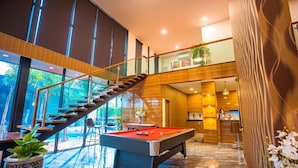 A modern interior with a pool table, wooden staircase, and a kitchen area.