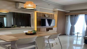 Un comedor moderno con una mesa de madera, sillas blancas, un televisor y una lámpara colgante decorativa.