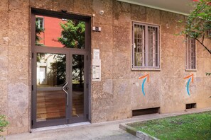 A building entrance with a glass door, stone walls, and a small window with metal bars.