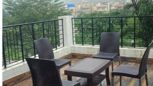 Een balkon met een houten vloer en zwart rieten meubilair, met uitzicht op een stadsgezicht met gebouwen en bomen.