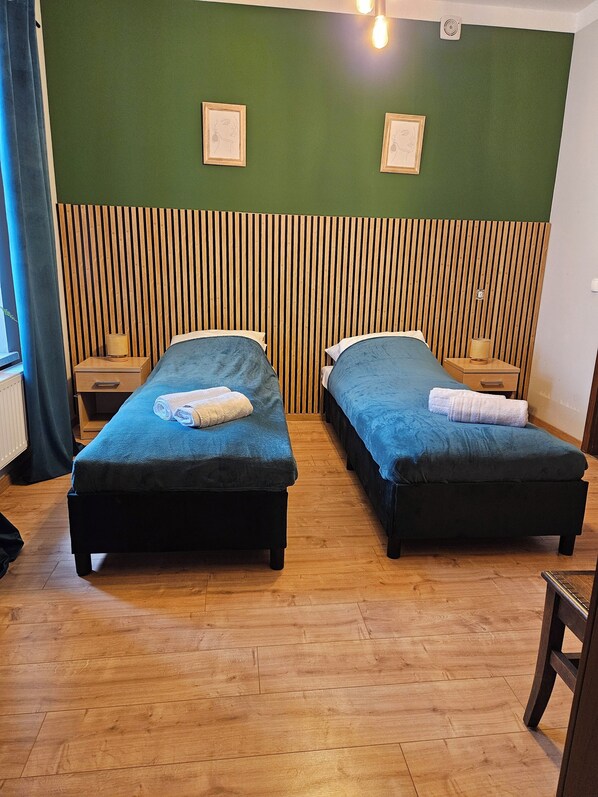 Habitación con dos camas, cabecero de listones de madera, paredes verdes y suelo de madera.