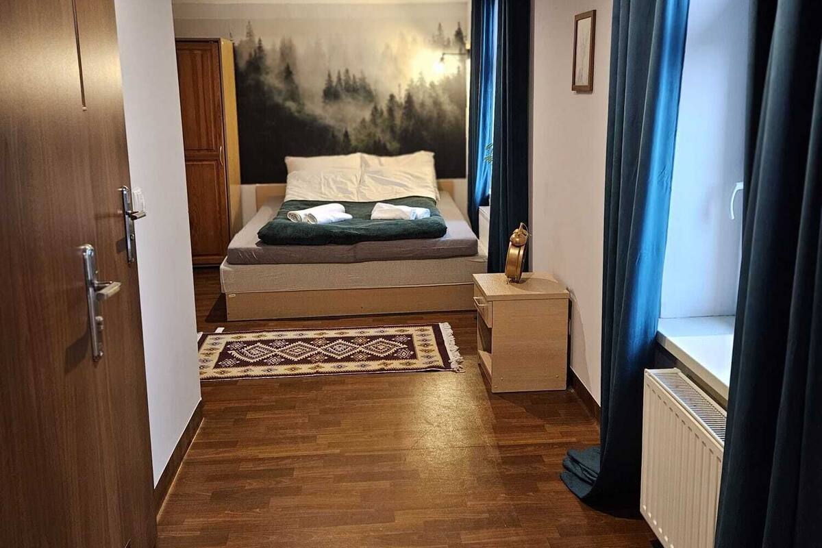 A bedroom with a bed, a nightstand, a dresser, a radiator, and a door.