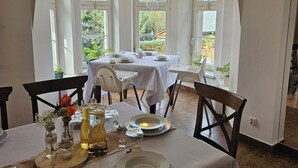 Comedor con una mesa lista para cuatro personas, manteles blancos y vistas a la vegetación exterior.