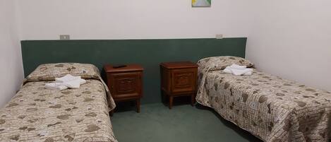 A room with two single beds, each with a floral-patterned bedspread, a wooden nightstand with a remote control, and a green headboard.