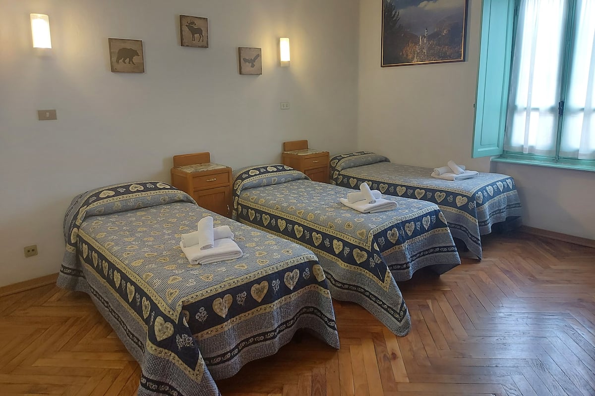 Une chambre avec trois lits, chacun agrémenté de draps à motifs de cœur, de tables de chevet en bois et de lampes fixées au mur.