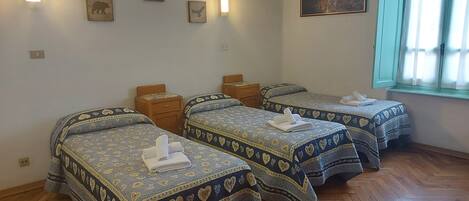 A room with three beds, each with heart-patterned bedding, wooden nightstands, and wall-mounted light fixtures.