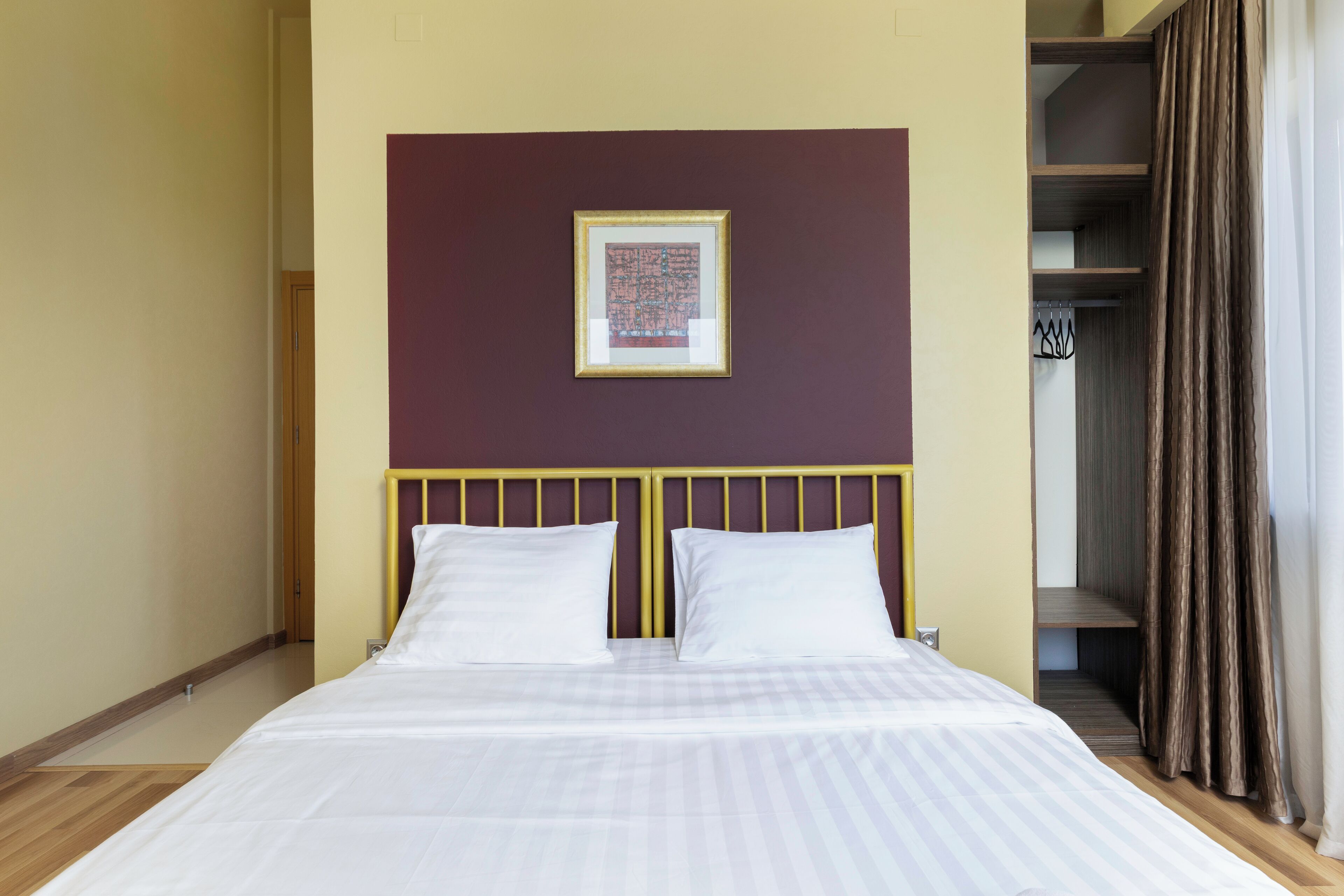 Una cama bien hecha con ropa blanca, un cabecero con marco dorado y un cuadro en la pared.