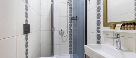 A modern bathroom with a glass-enclosed shower, white tiles, and a white sink with a mirror above it.