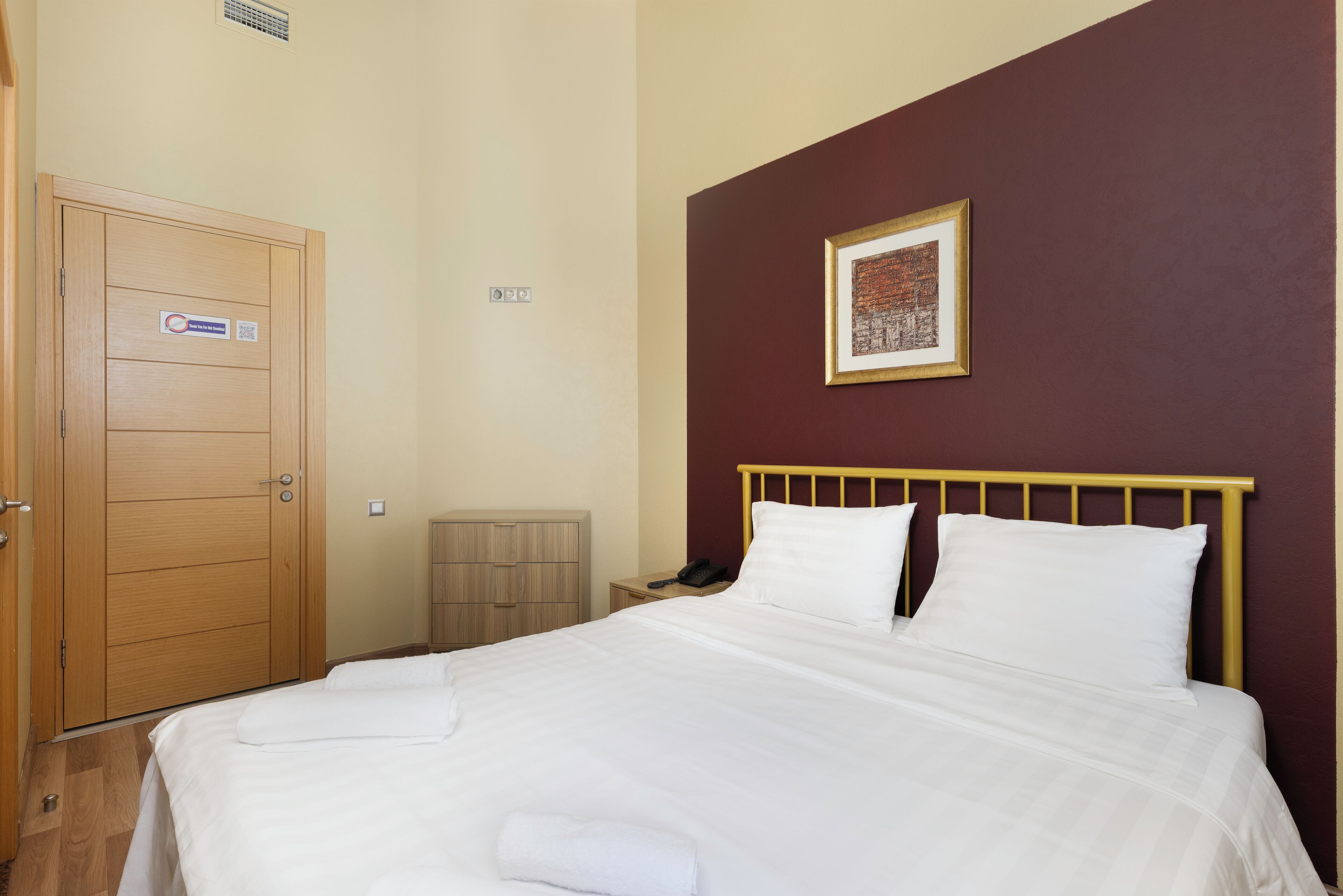A neatly made bed with white linens, a wooden headboard, and a framed picture on the wall.