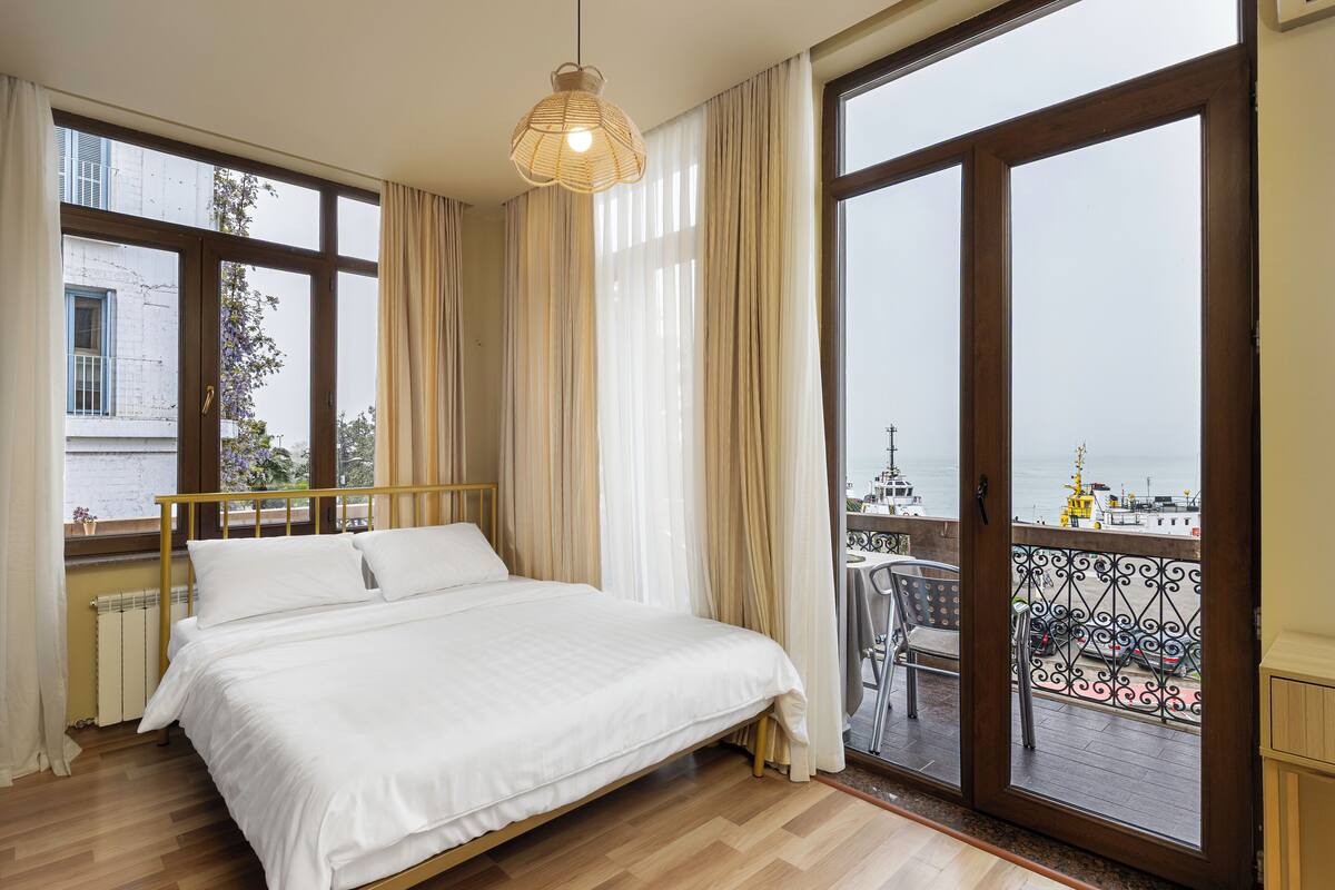 Quarto com uma cama grande, vista para o mar e varanda com área de estar externa.
