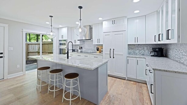 Una cocina moderna con armarios blancos, una isla grande con taburetes y vistas al exterior.