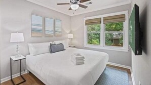 Habitación de hotel con cama, ventilador de techo, ventana con vistas y televisor de pantalla plana montado en la pared.