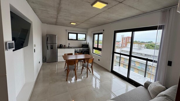 Un apartamento moderno con cocina, comedor y sala de estar. Cuenta con ventanas amplias, un balcón y televisor de pantalla plana.