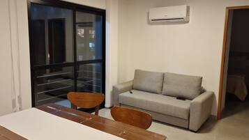 Una sala de estar con sofá, una mesa de comedor y sillas. Hay una puerta corrediza de vidrio que da a un balcón.