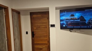 Un pasillo con una puerta de madera y un televisor en la pared que muestra un juego.
