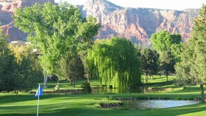 A golf course with a pond, trees, and mountains in the background.