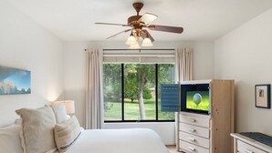 A bedroom with a bed, a TV, a desk, and a window with a view of a golf course.