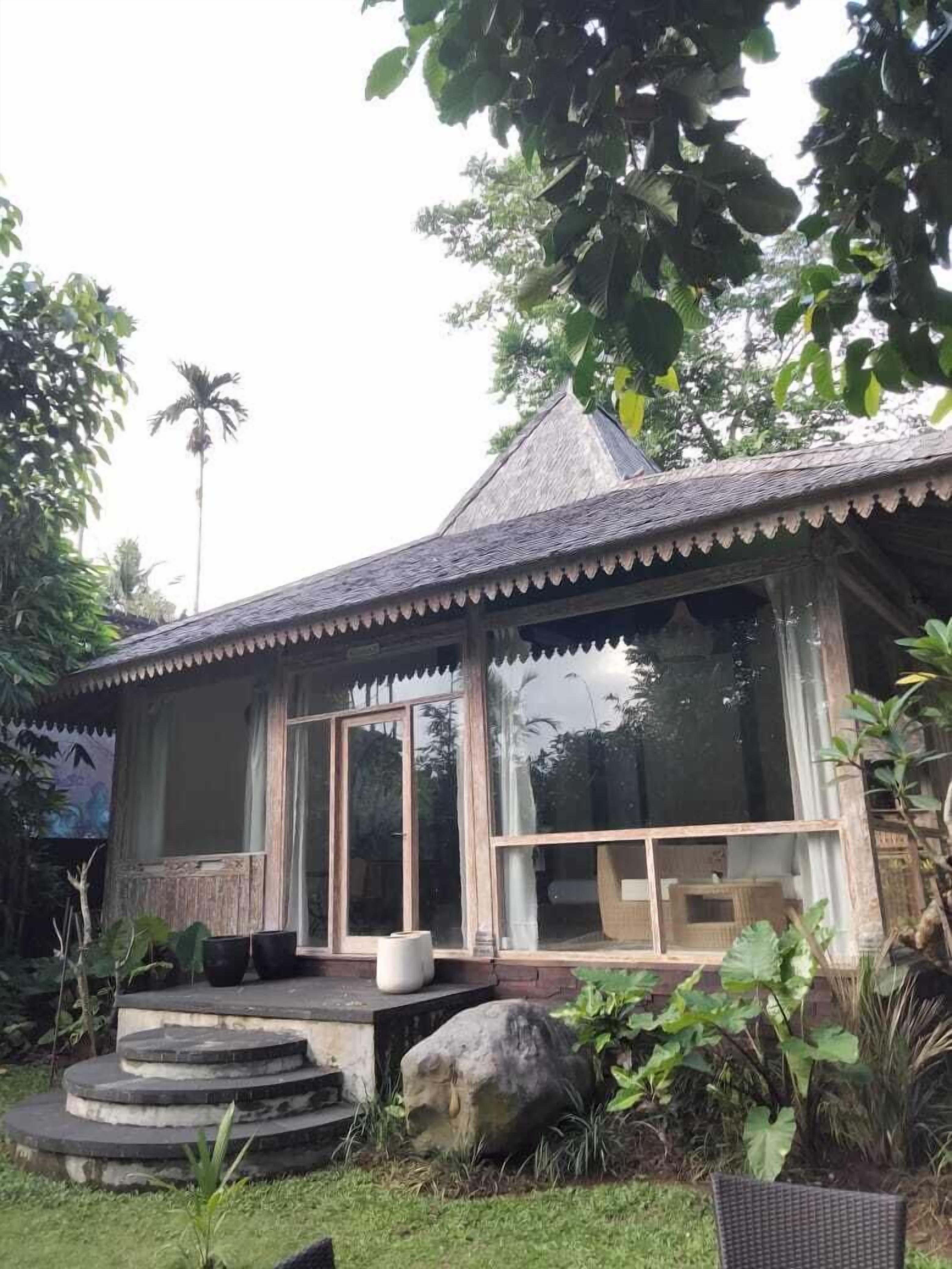 Una casa de madera tradicional con techo de paja, ventanas grandes y una escalera de piedra que lleva a la entrada.
