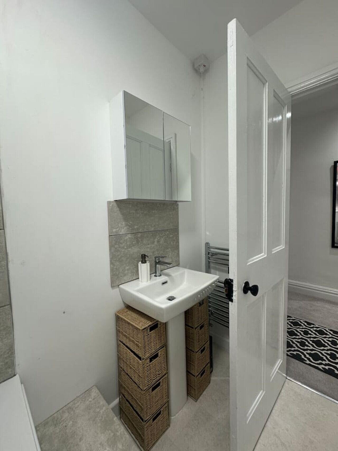 A bathroom with a white sink, a mirror, and a door leading to another room.