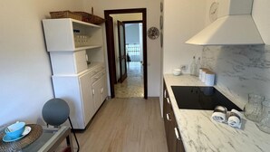 Eine kleine Küche mit Kühlschrank, Spüle und Arbeitsplatte. Eine Tür führt zu einem Balkon.