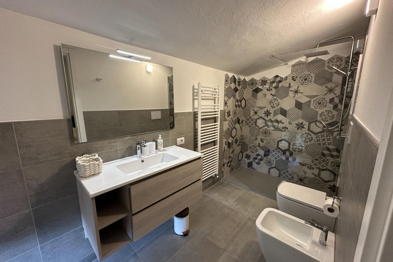 A modern bathroom with two sinks, a large mirror, a shower with a glass door, and patterned tiles on the walls.