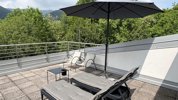 Eine Dachterrasse mit Liegestühlen, einem Tisch und einem Sonnenschirm.