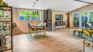 Un vaste salon doté d’un plancher en bois, un coin repas avec une table et des chaises, une cheminée et un téléviseur fixé au mur.