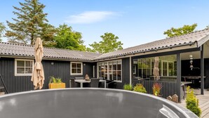 Un espace moderne aménagé à l’extérieur avec un bain à remous, une terrasse en bois, un coin salon abrité et une grande fenêtre donnant sur l’ensemble de l’espace.