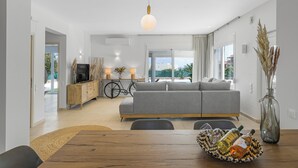 A modern living room with a sofa, dining table, and a bike in the background. - Villa Yiayia: Relaxing by the sea (Heated pool) (Sisi)