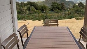 Un patio exterior con mesa y sillas de madera, con vista a un paisaje pintoresco con colinas y una ciudad distante.